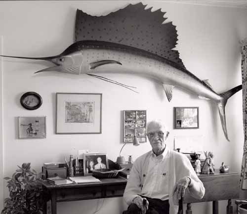 Man sitting at a desk with a large swordfish above, on the wall