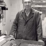 Man wearing a coat with "Everett" on it at a working bench with a saw in it